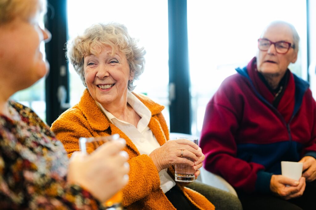 Three older friends laughing and talking together over drinks