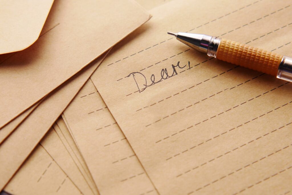 Handwritten letter beginning with "Dear," on kraft paper with a pen resting on it