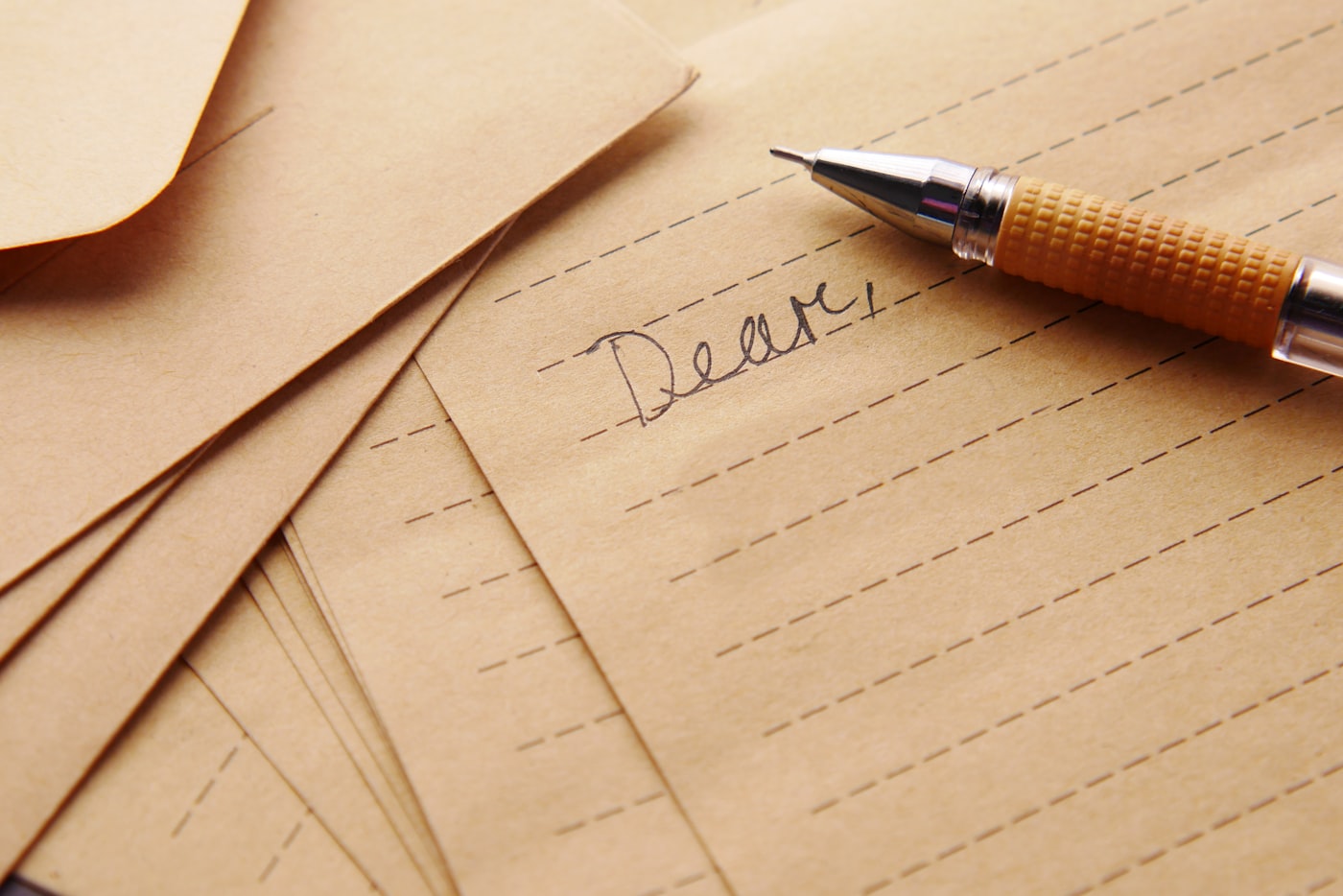 Handwritten letter beginning with "Dear," on kraft paper with a pen resting on it