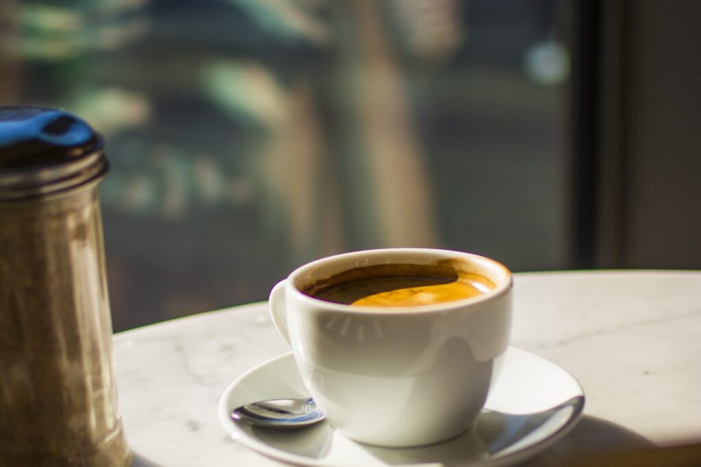 A cup of coffee on a sunlit café table in the early morning light